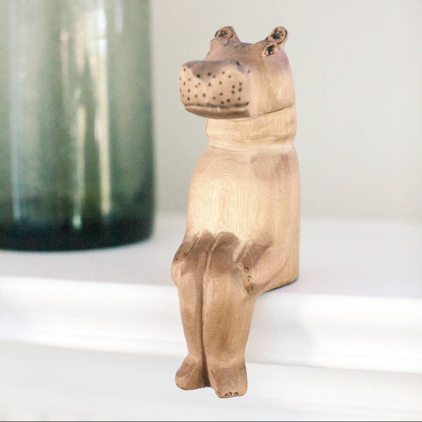 Wooden hippo figurine on a shelf ledge with a blurred green container in the background