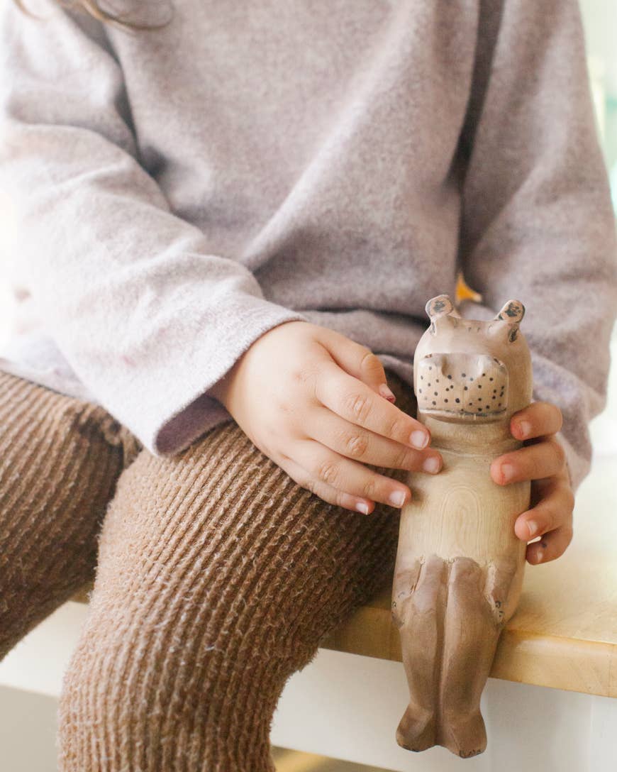 Person holding a wooden elephant ledge lounger with a child's legs and sweater in the foreground.