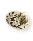 Decorative ceramic dish with black floral patterns holding gold hoop earrings on a white background