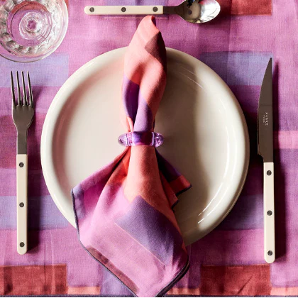 Table setting with a plate, fork, knife, and colorful napkin on a pink checkered tablecloth.