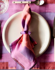 Table setting with a plate, fork, knife, and colorful napkin on a pink checkered tablecloth.