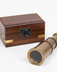 Mini brass telescope with an antique finish displayed next to its velvet-lined wooden storage box on a neutral surface.