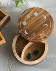 Wooden jewelry box with moon phase design on lid, containing green earrings.