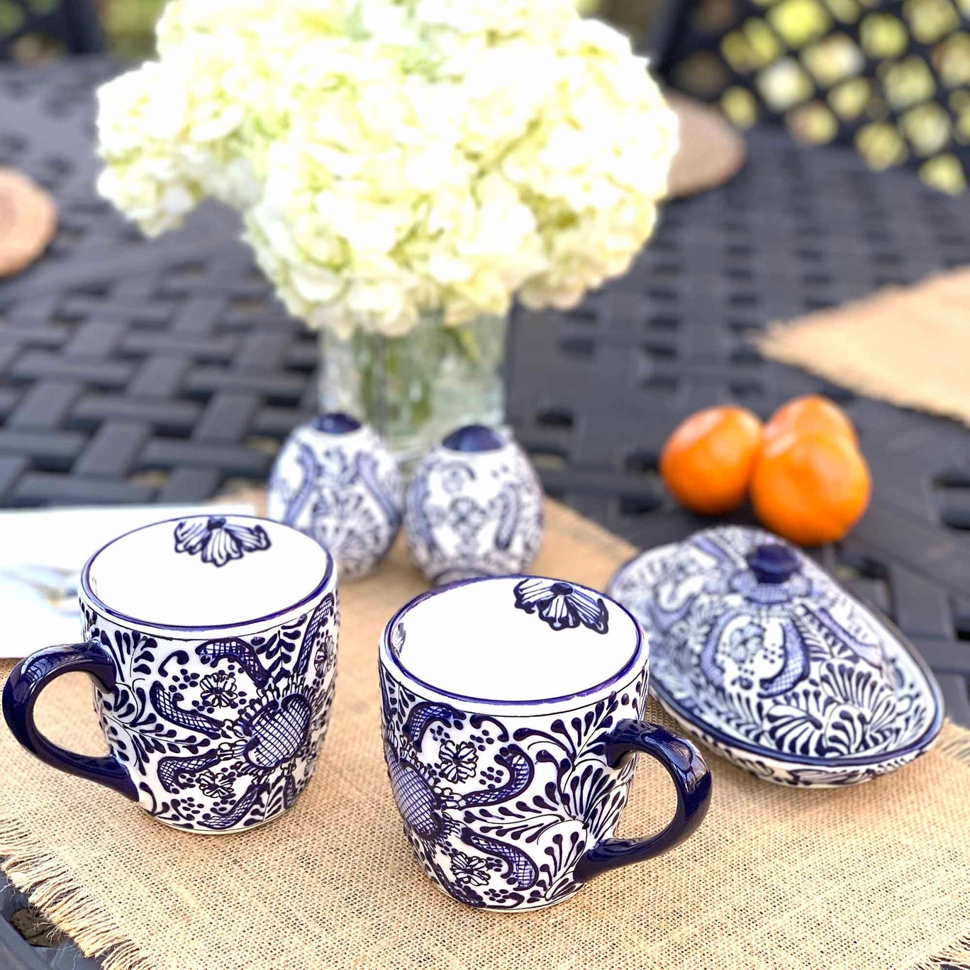 Blue and white ceramic mugs with floral patterns on a table with flowers and oranges.