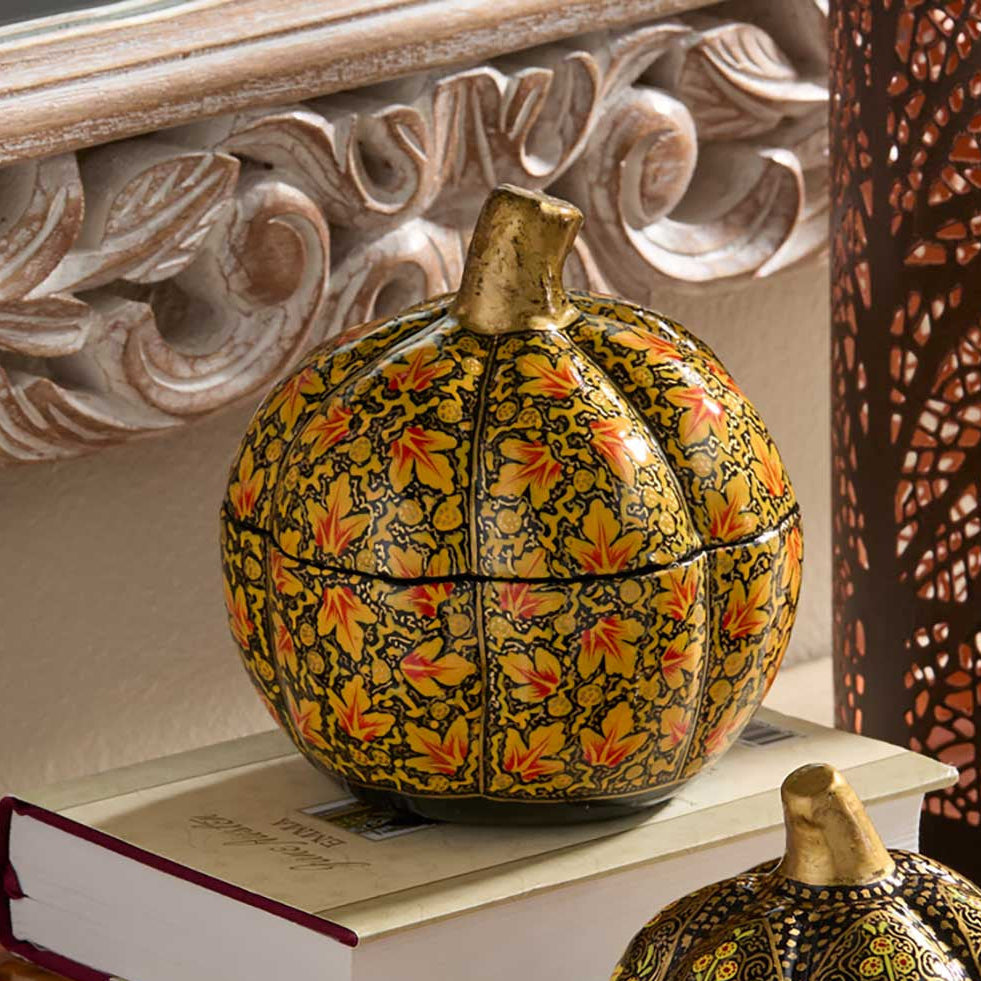 Two decorative pumpkin-shaped boxes with intricate floral patterns, displayed on stacked books in a styled indoor setting.
