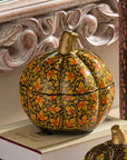 Two decorative pumpkin-shaped boxes with intricate floral patterns, displayed on stacked books in a styled indoor setting.