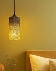 Decorative pendant light hanging above a bed with a warm glow on a yellow wall.