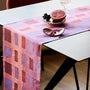 Table with a pink and purple checkered tablecloth, fruit on a plate, and a glass of white wine.