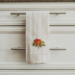 Tea towel with a pumpkin design hanging on a kitchen cabinet