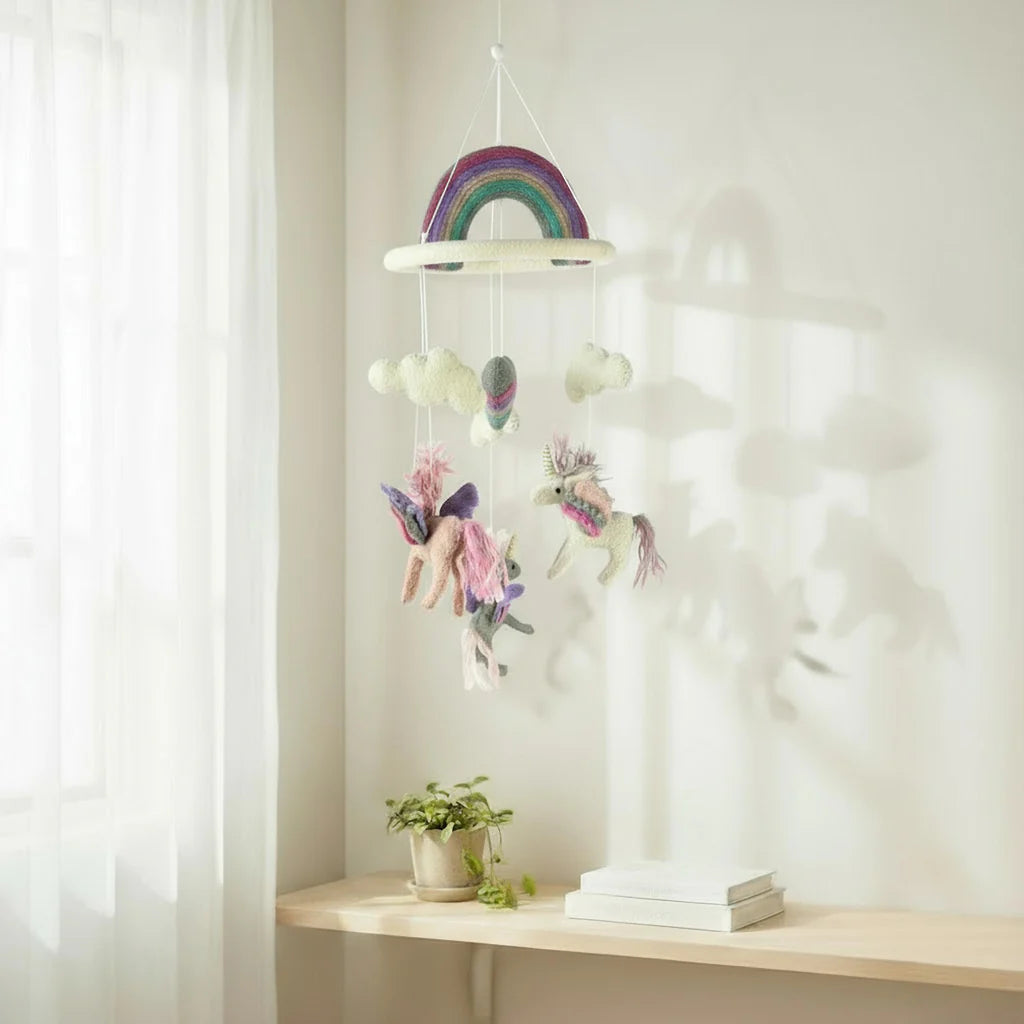 Children's mobile with rainbow and fairy design hanging above a shelf.
