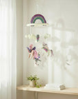 Children's mobile with rainbow and fairy design hanging above a shelf.