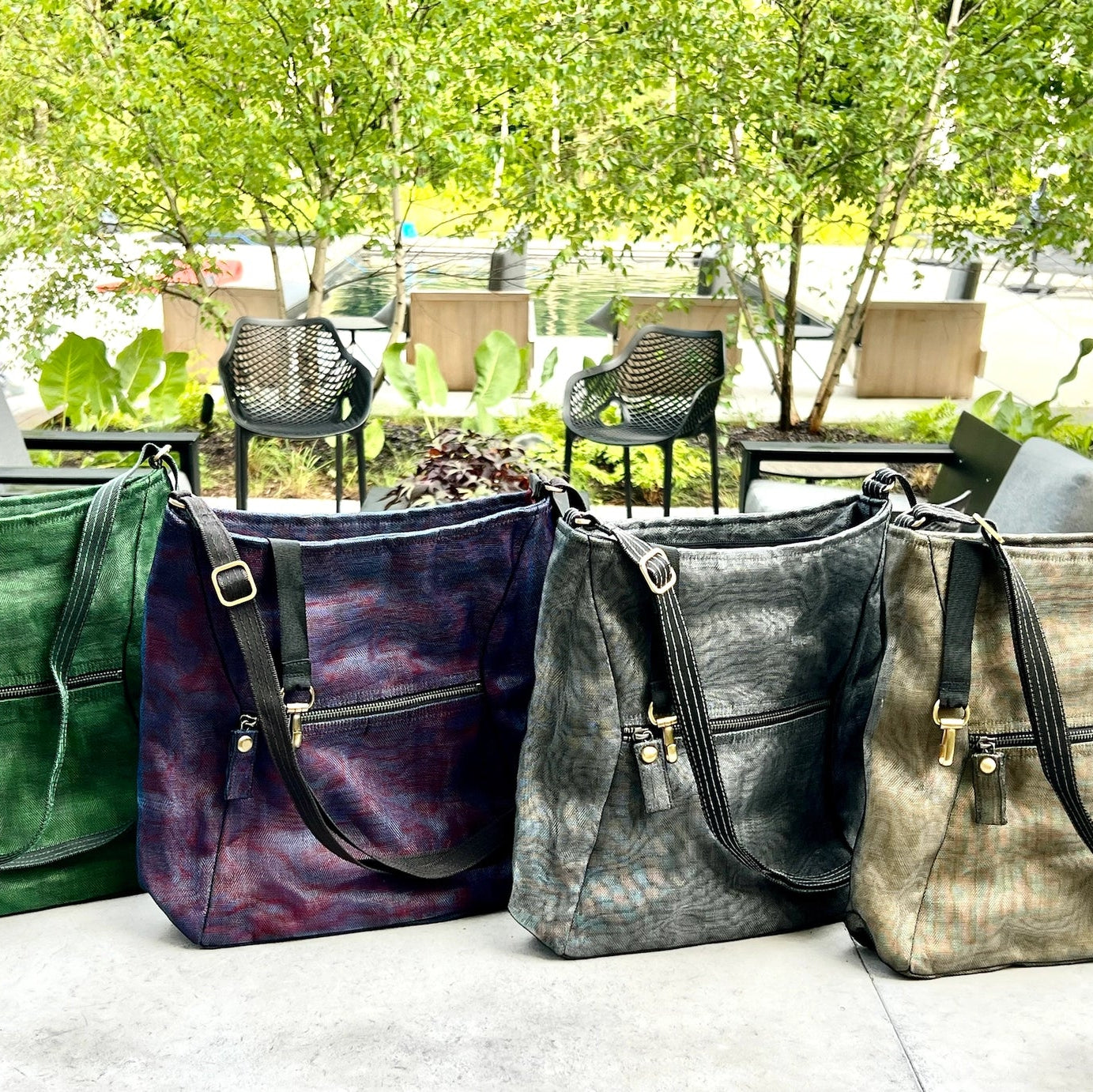 Four handbags in different colors on a surface with a blurred outdoor background