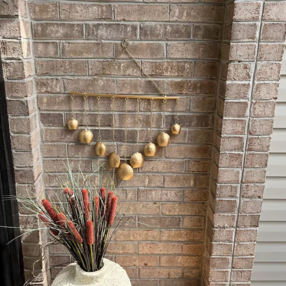 Decorative gold balls hanging on a brick wall with a vase of red flowers in the foreground.