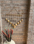 Decorative gold balls hanging on a brick wall with a vase of red flowers in the foreground.