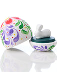 Decorative egg with floral patterns and a small rabbit figure on a reflective surface
