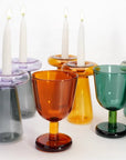 Colorful glass candle holders with white candles on a white background