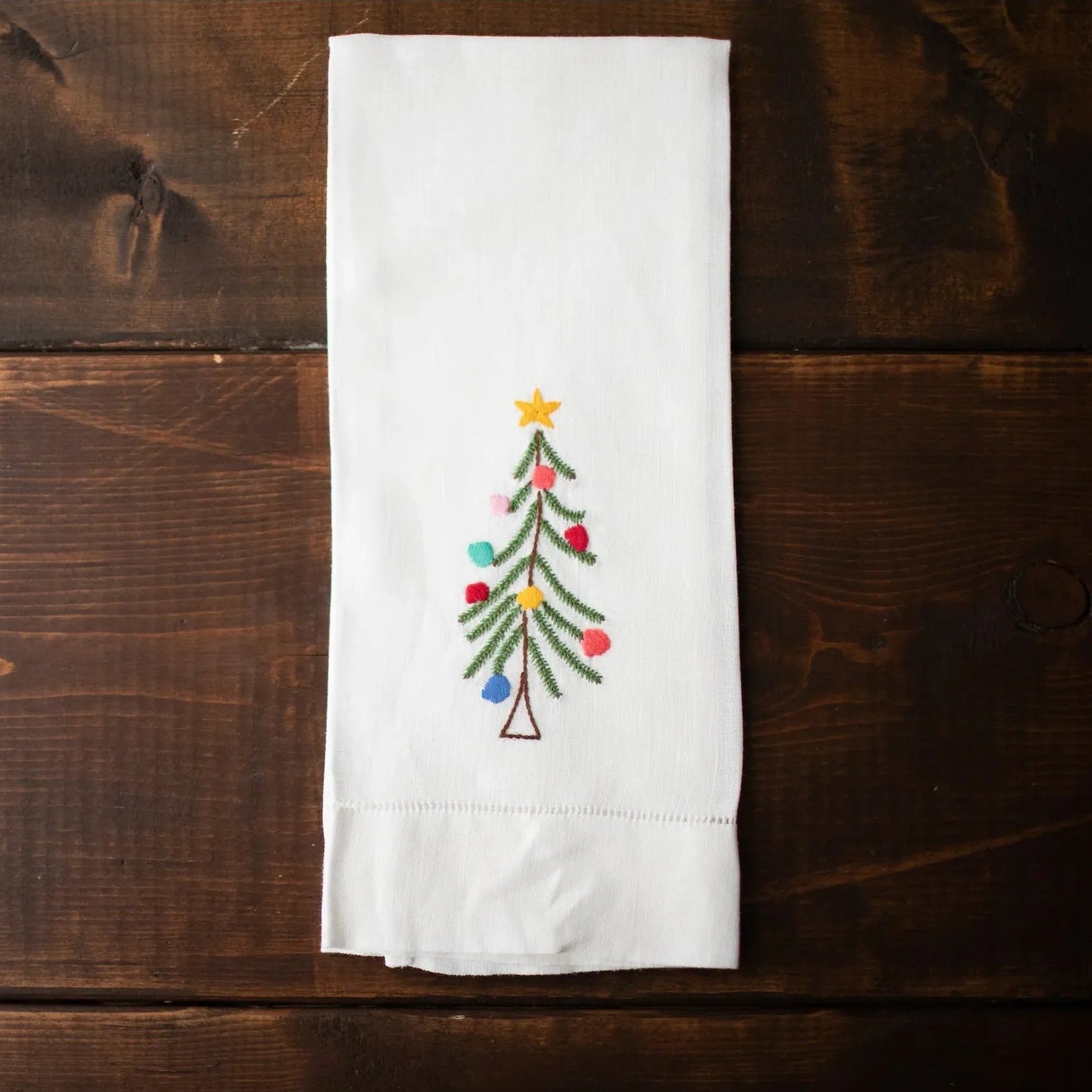 White tea towel with a embroidered Christmas tree design on a wooden surface