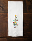 White tea towel with a embroidered Christmas tree design on a wooden surface