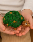 Green textured turtle figurine held in hands against a neutral background