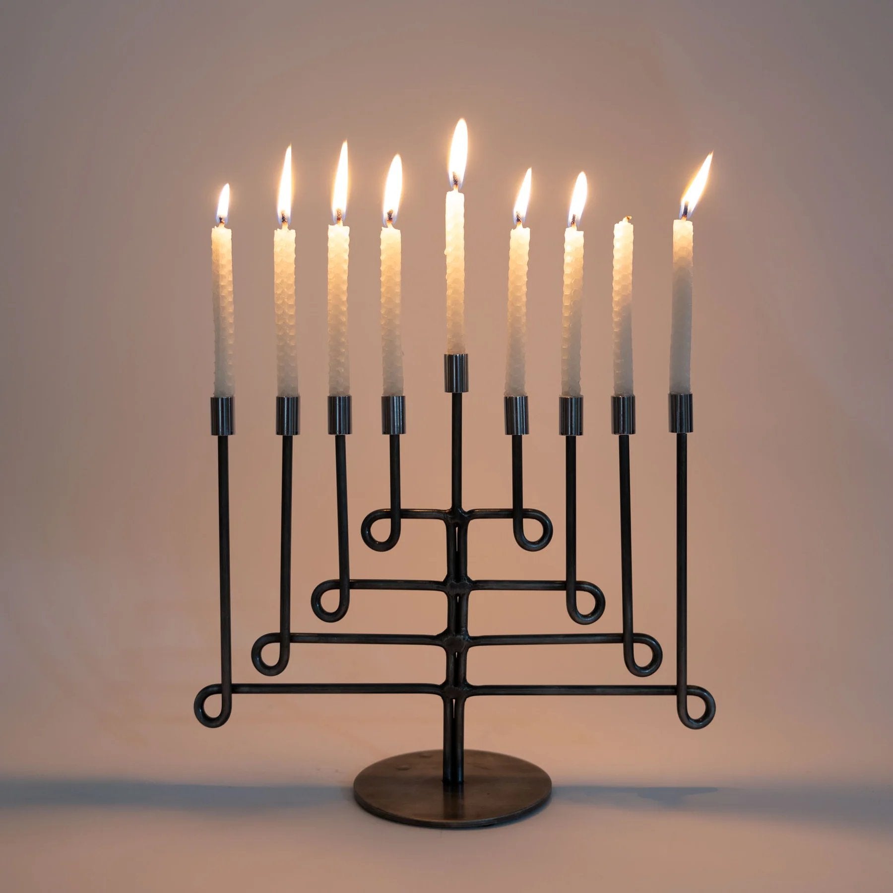 Black metal menorah with lit candles on a plain background