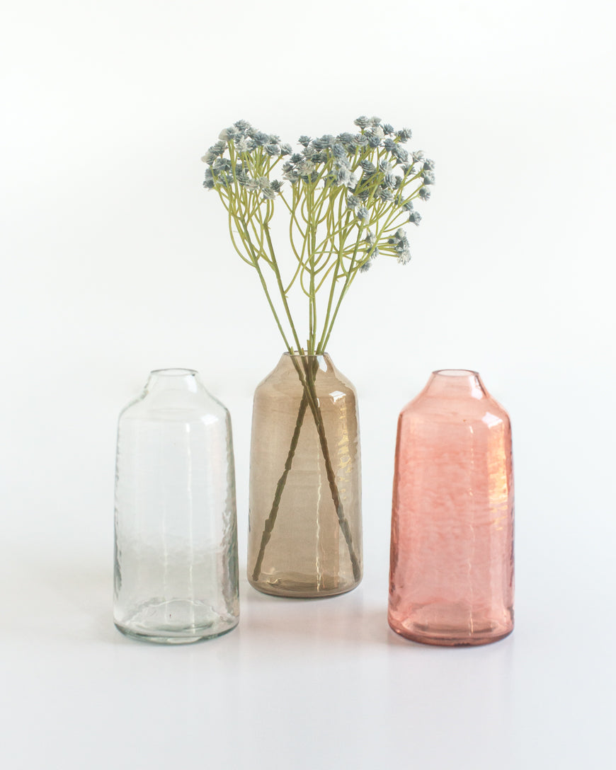 Three glass vases of different colors with a single stem of flowers on a white background
