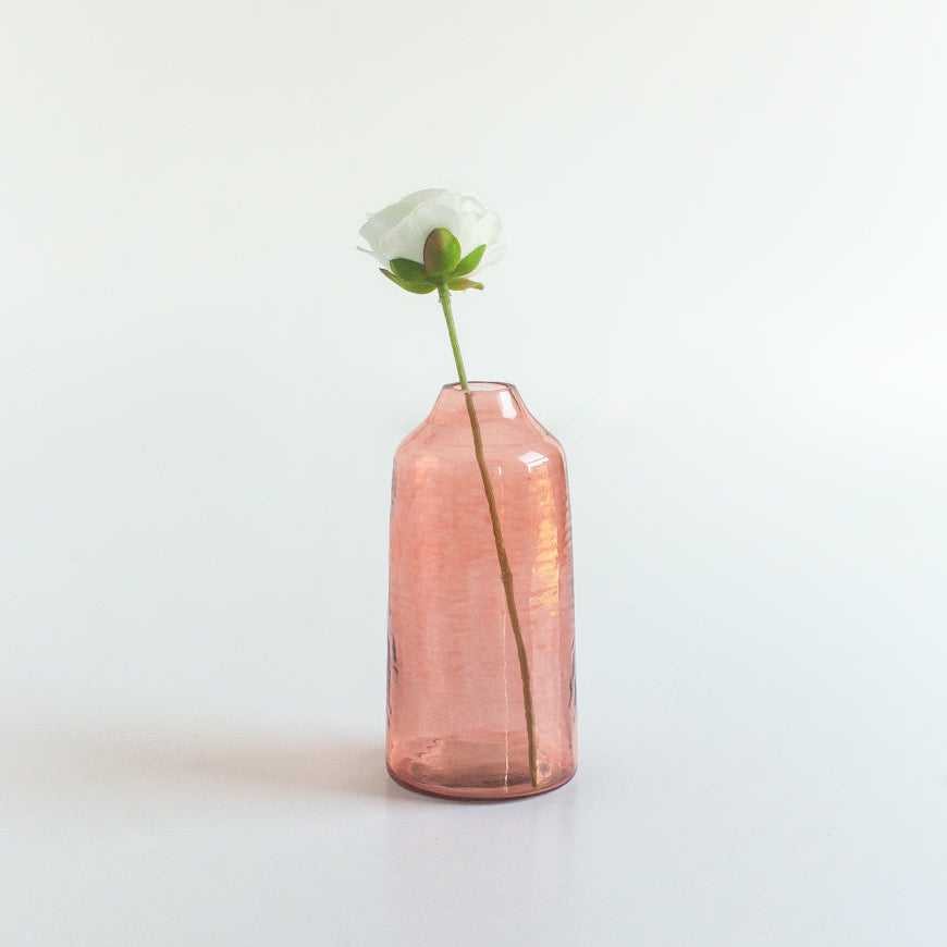 Pink glass vase with a white flower on a light gray background