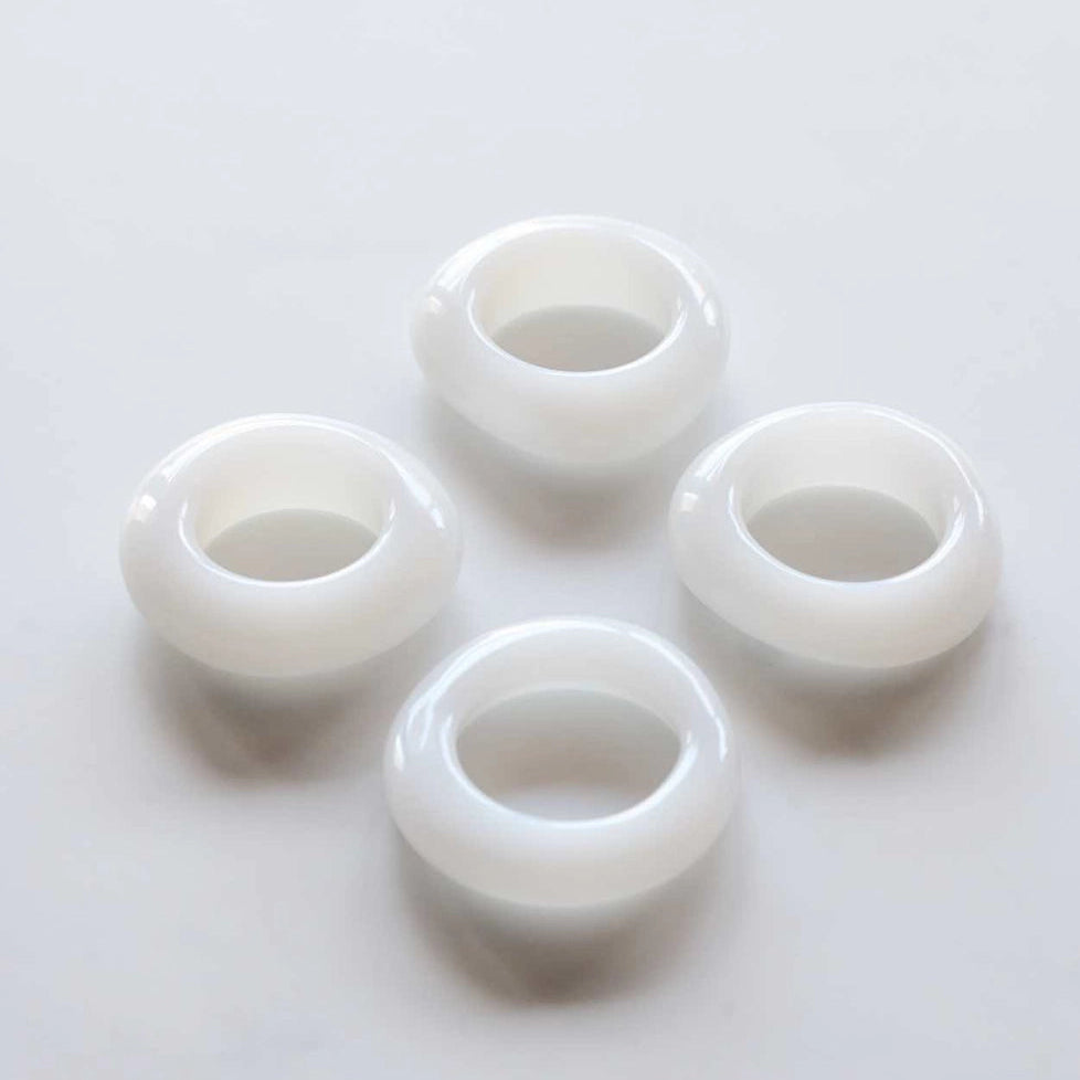Four white glass napkin rings on a light gray background