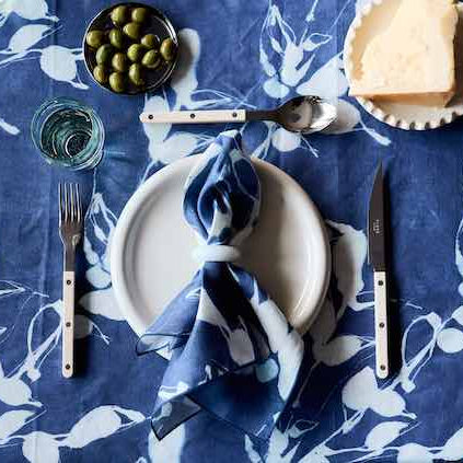 Table setting with a blue floral tablecloth, white plates, silverware, and a blue napkin.