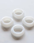 Four white glass napkin rings on a light gray background