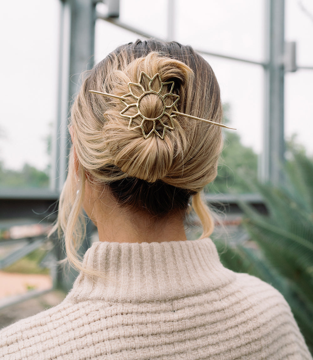 Person with blonde hair styled in an updo with a decorative hairpin, wearing a beige sweater.