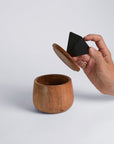 Wooden cup with a hand holding a black triangle-shaped object on a light gray background