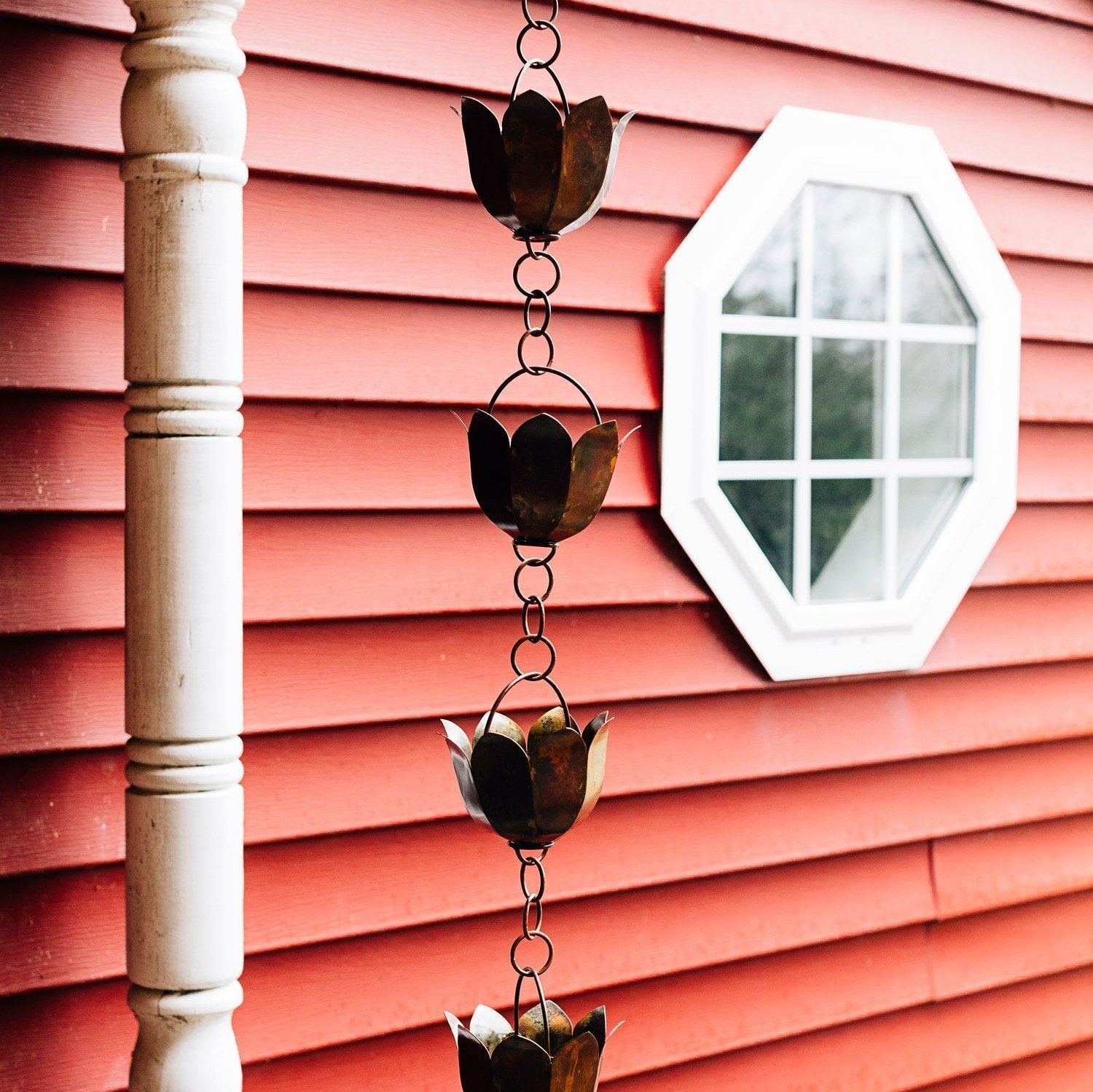 Decorative metal rain chain on a pink wooden wall with a small mirror.