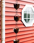 Decorative metal rain chain on a pink wooden wall with a small mirror.
