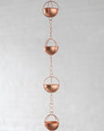 Copper rain chain with spherical design on a light gray background