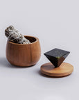 Wooden container with smudge stick and black geometric sculpture on a light gray background
