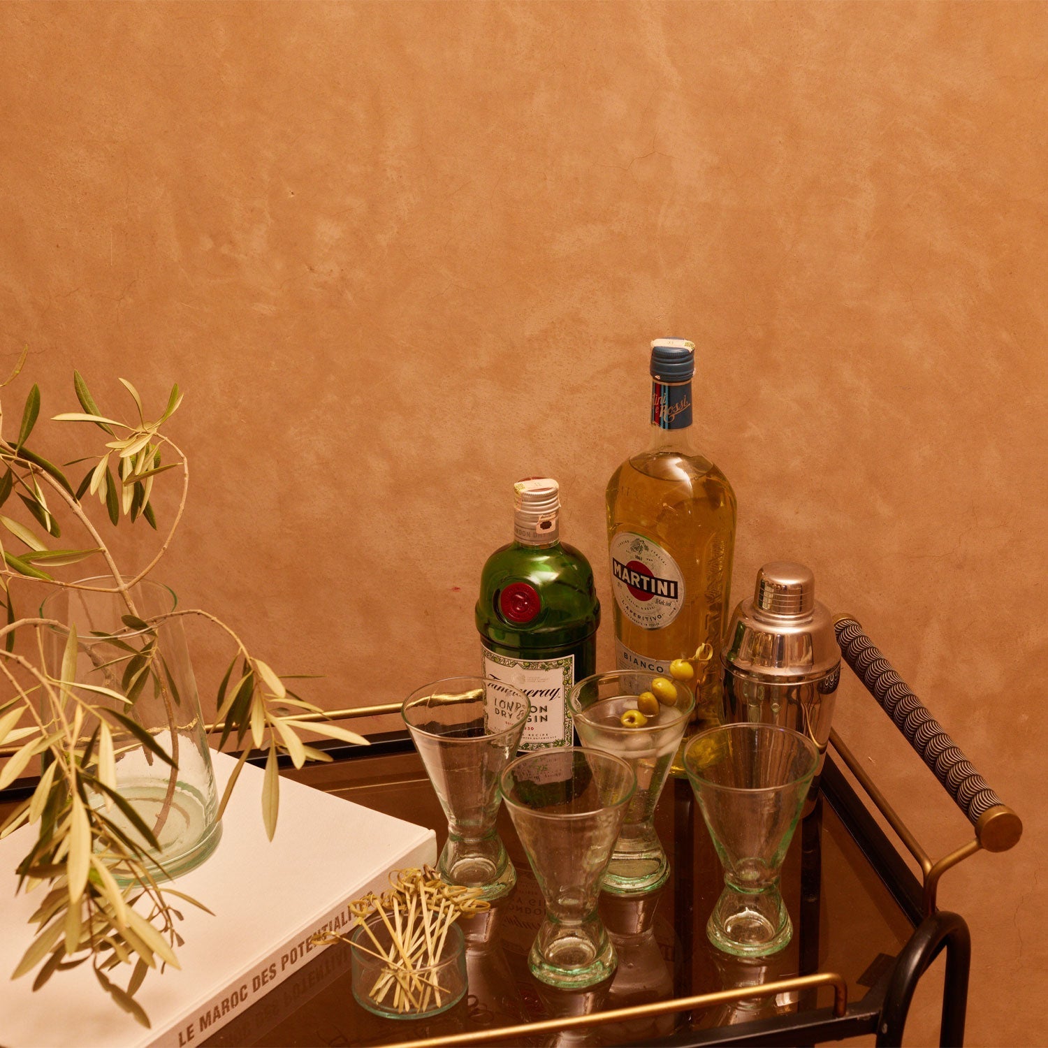 Bar cart with cocktail ingredients and tools against a brown wall
