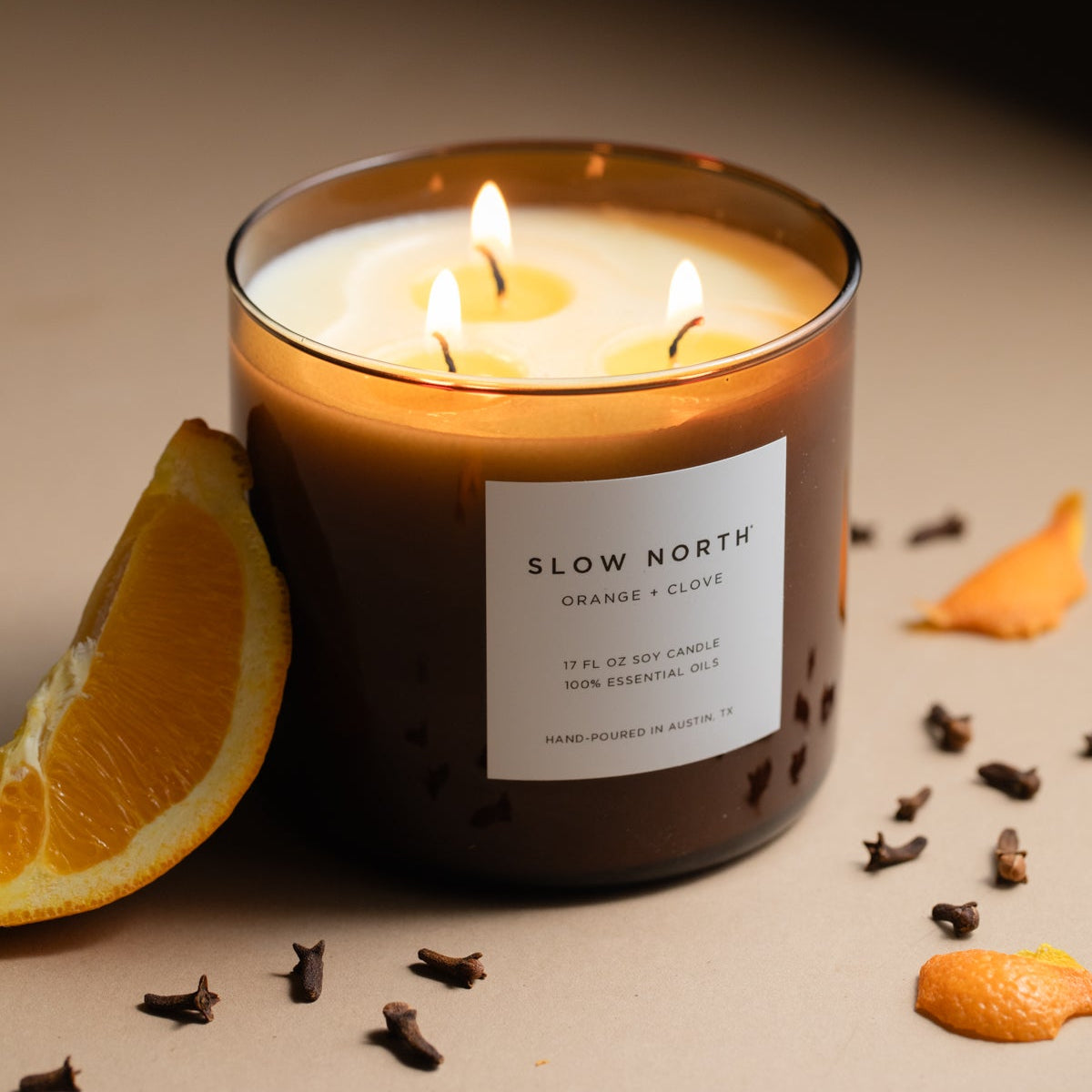 Scented candle labeled 'Slow North' with orange and clove elements on a neutral background