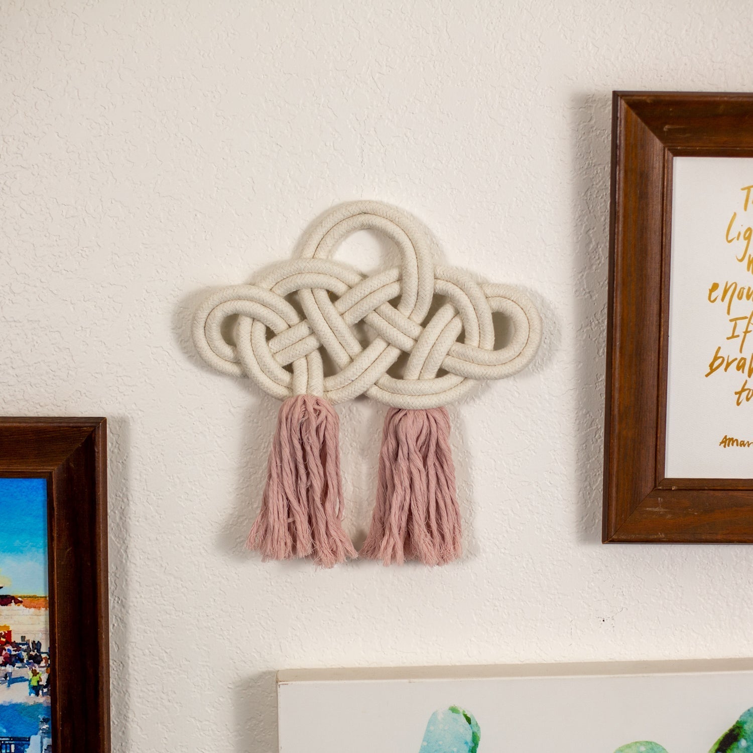 Decorative cotton wall piece with braided design and tassels on a wall next to framed pictures