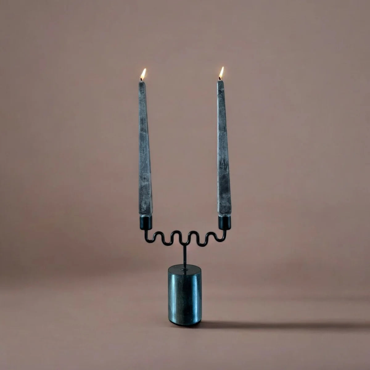 Modern gothic candle holder with two lit candles on a beige background