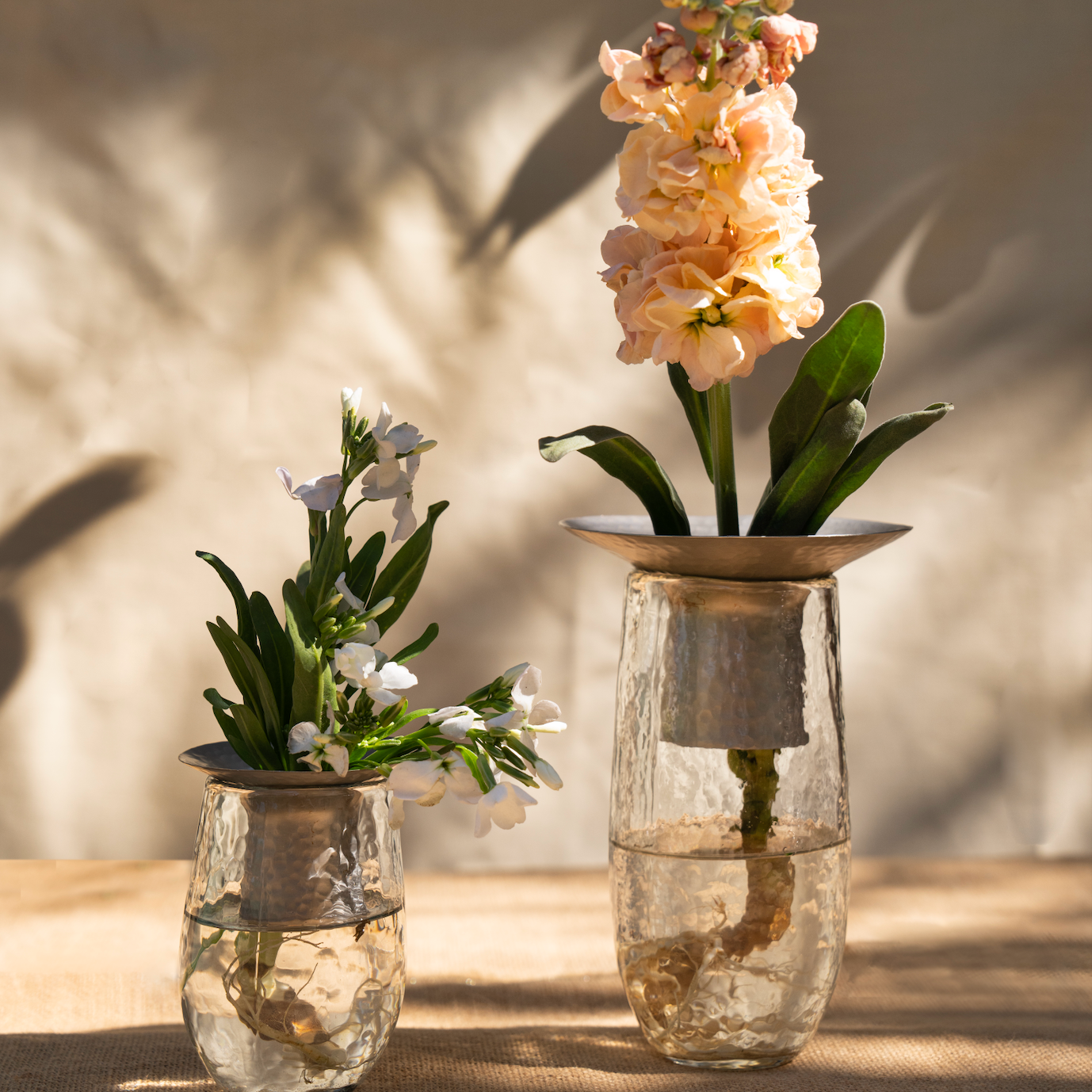 Two glass vases with flowers on a wooden surface with a neutral background