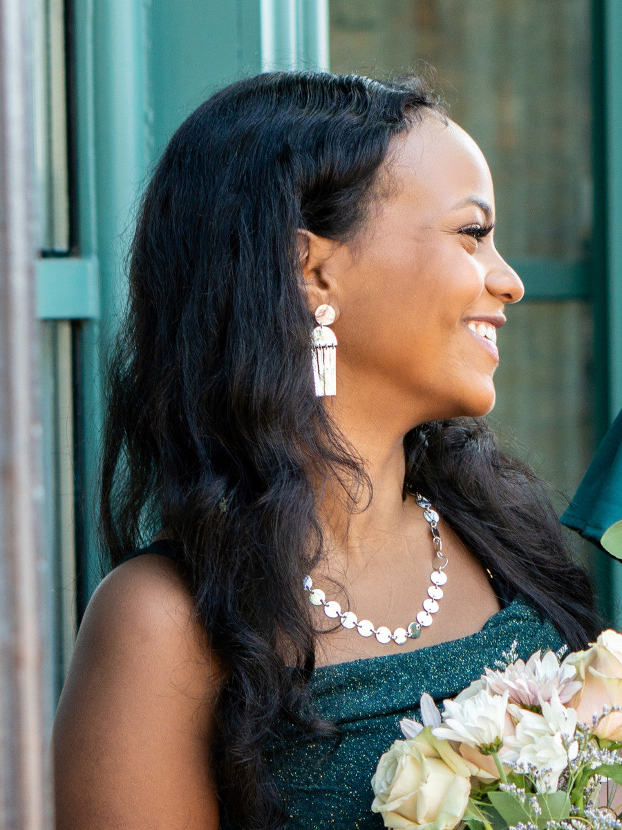 Woman with long dark hair holding a bouquet of flowers, wearing a green dress and silver jewelry.