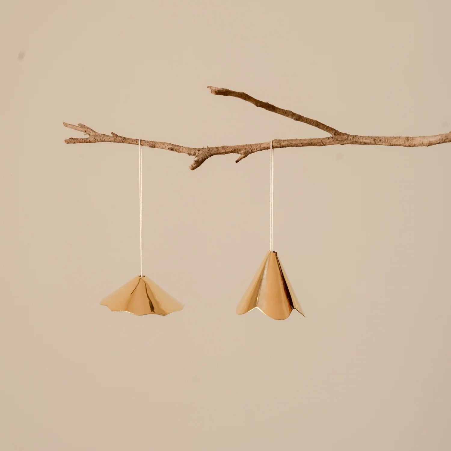 Two brass ornaments hanging from a branch against a beige background