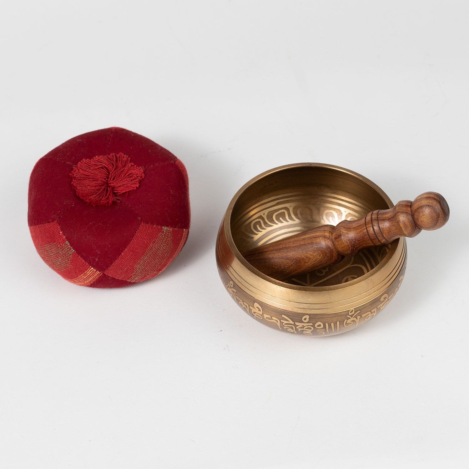 Brass singing bowl with wooden handle and red cushion on a white background