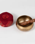 Brass singing bowl with wooden handle and red cushion on a white background