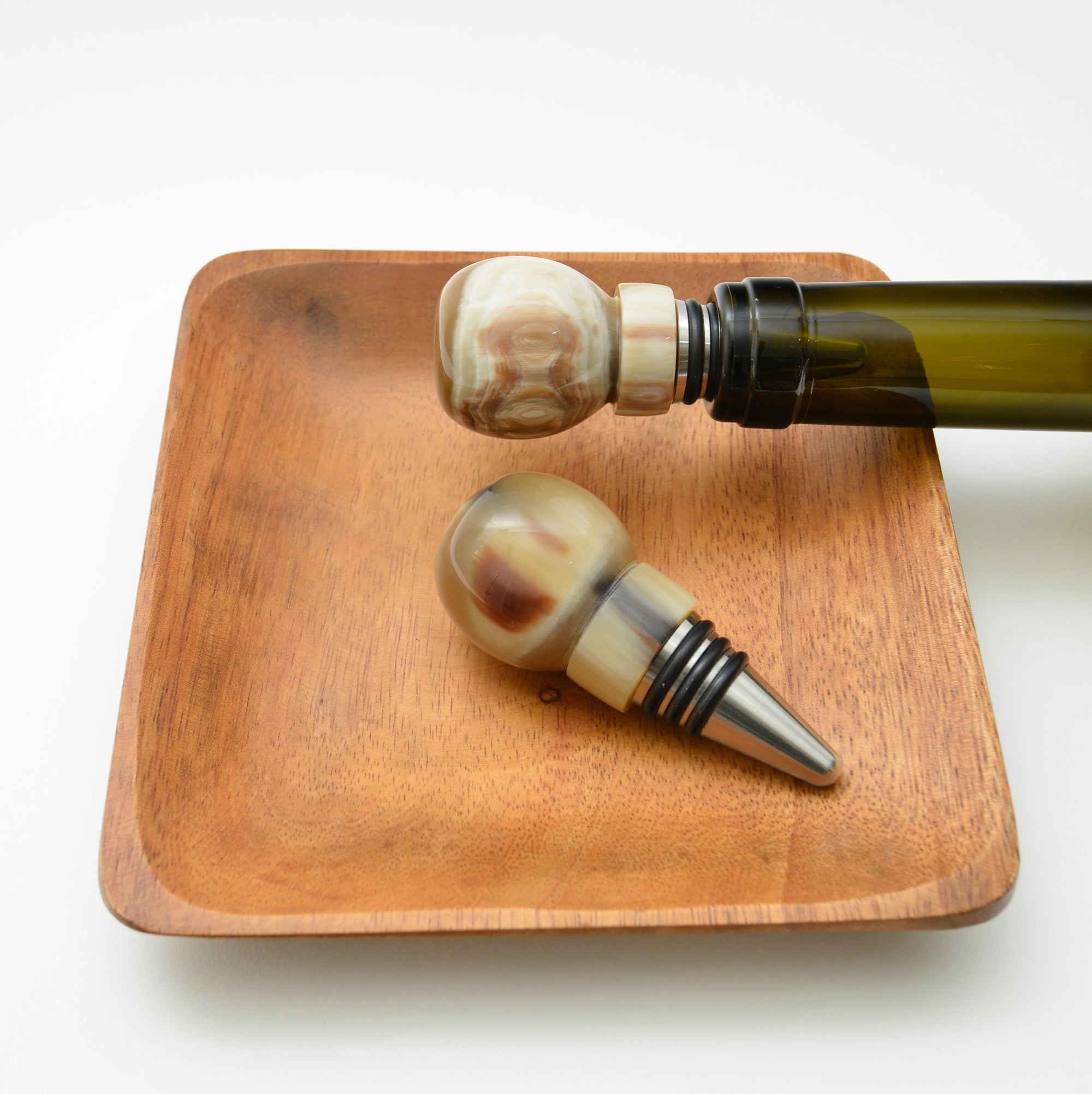 Two decorative bottle stoppers on a wooden tray with a white background