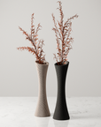 Two tall vases with textured designs and dried plants on a light background