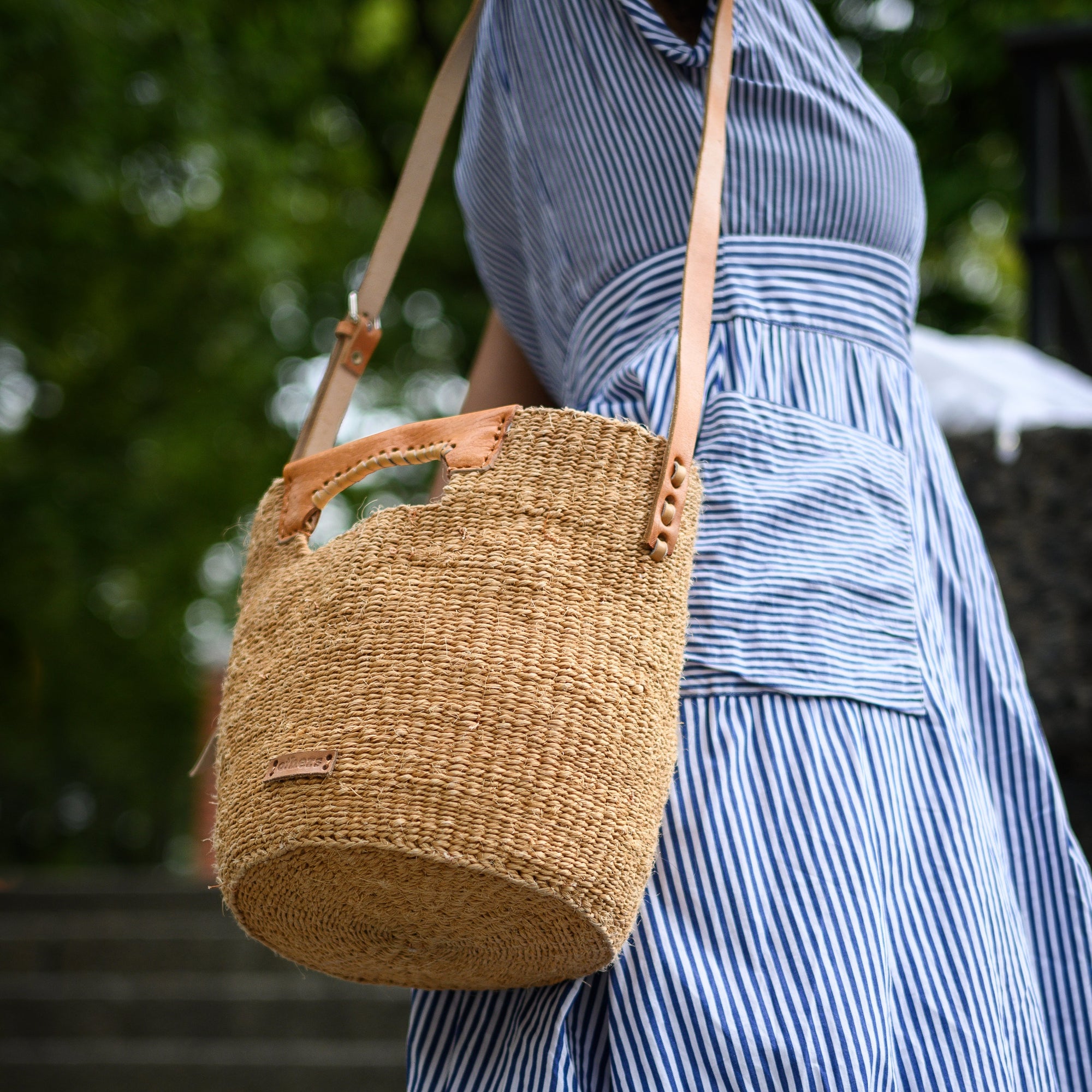 Person wearing a blue striped dress with a woven basket bag outdoors.