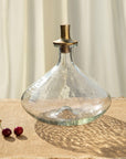 Clear glass decanter with a gold stopper on a textured surface with two cherries.