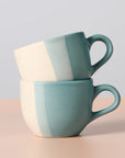 Two ceramic mugs with a two-tone design stacked on a light background