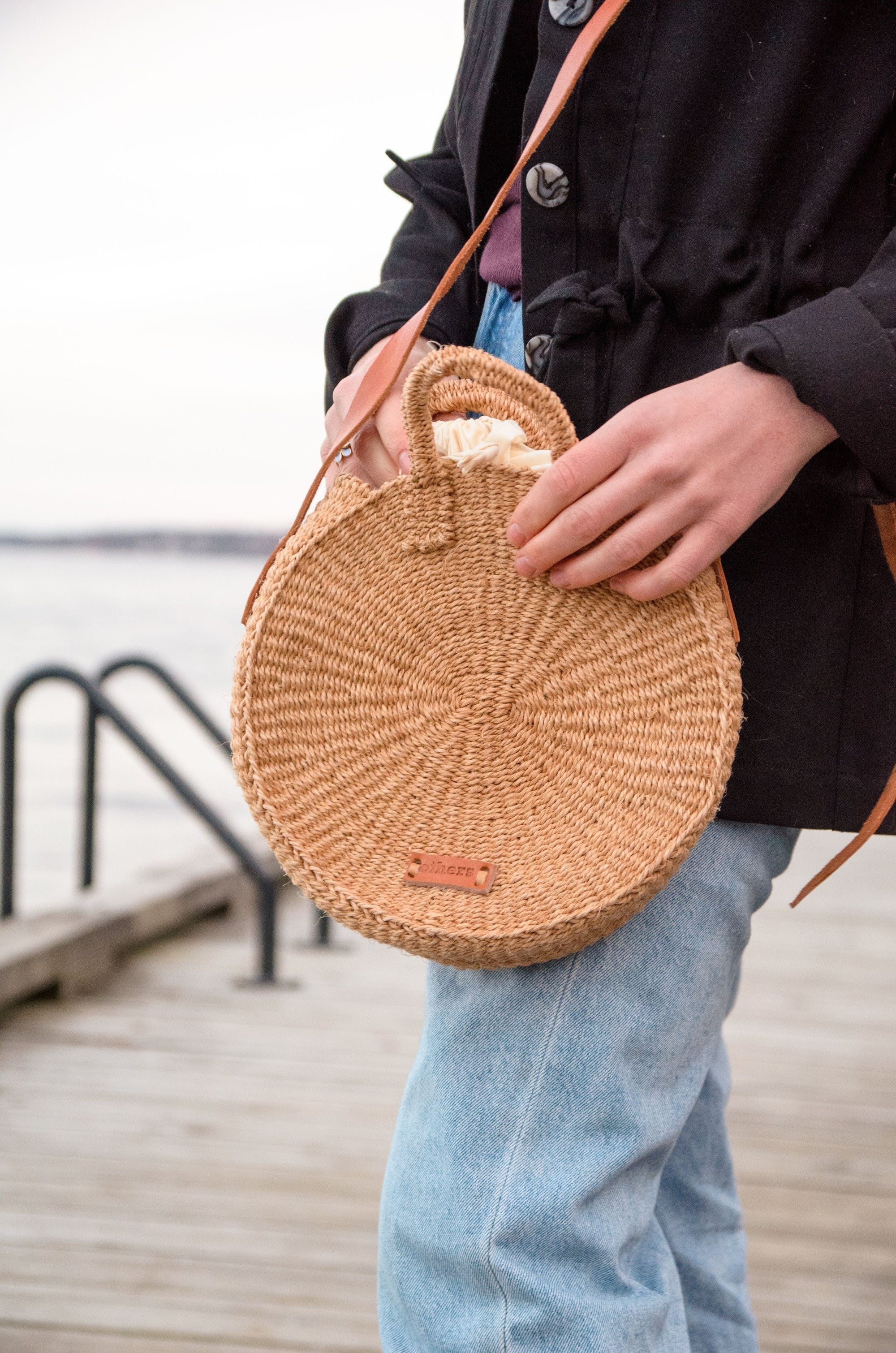 Person holding a round woven bag by a waterfront
